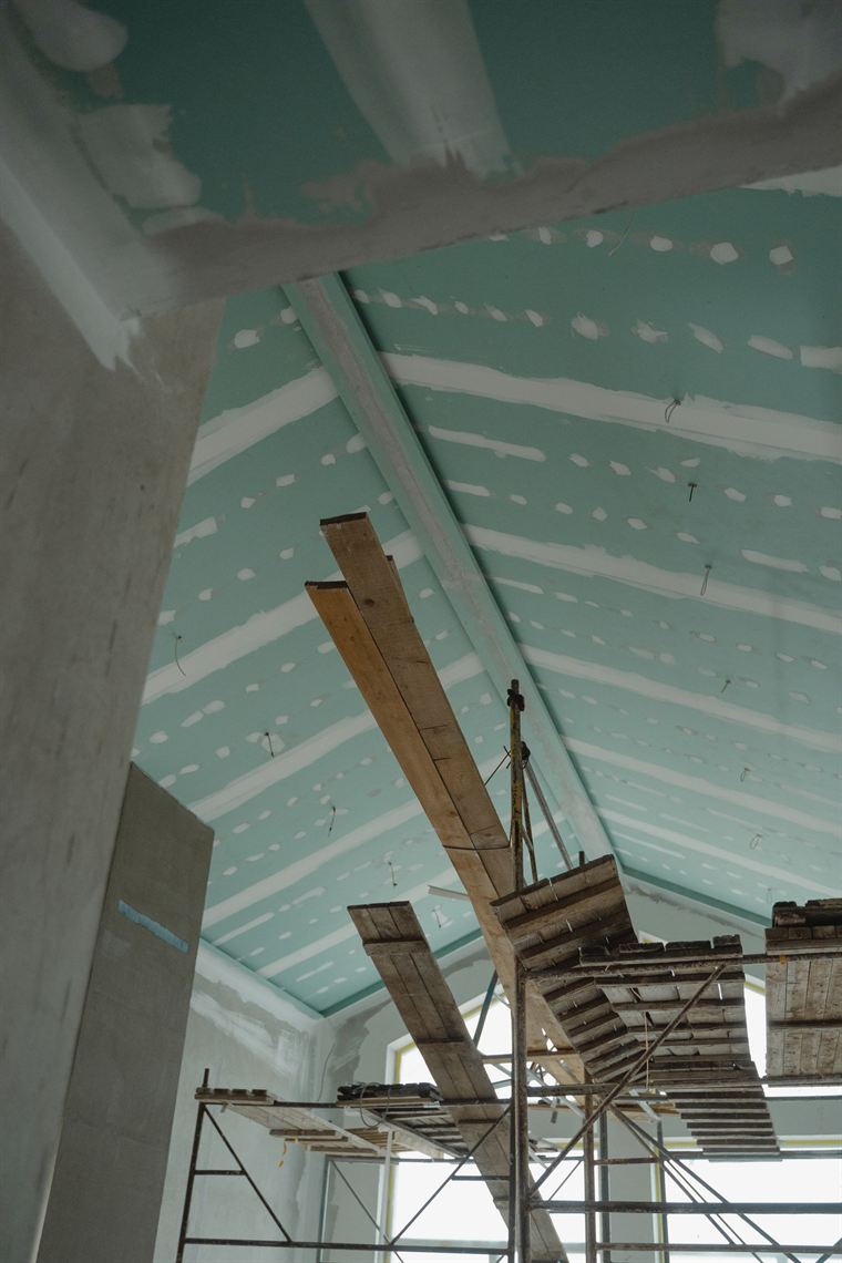 Green moisture-resistant plasterboard being fixed to ceiling framing
