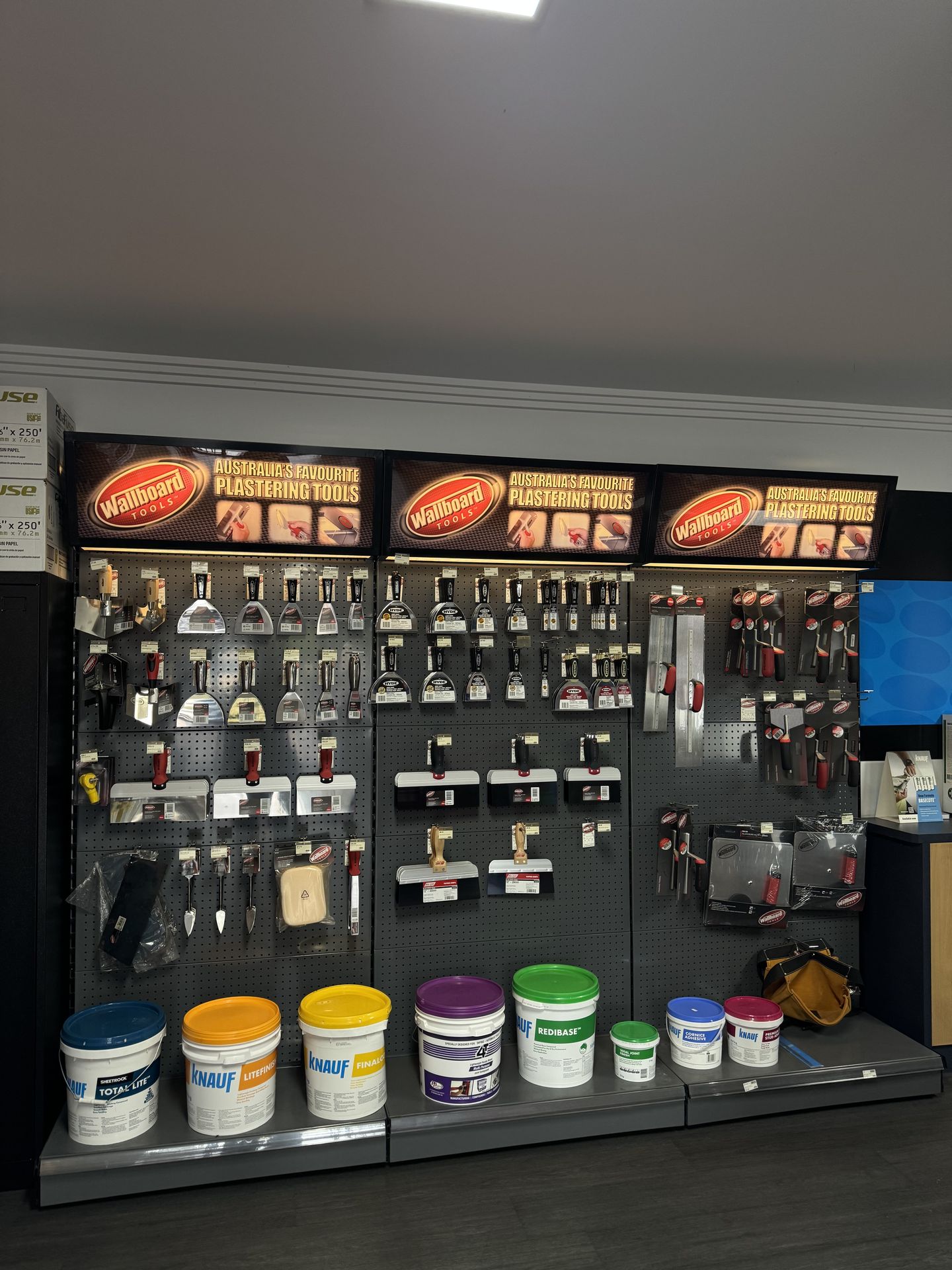 Wallboard Tools trowel and blade display with a row of Knauf compound buckets (Total Lite, Litefinish, Finalcote, Rediba